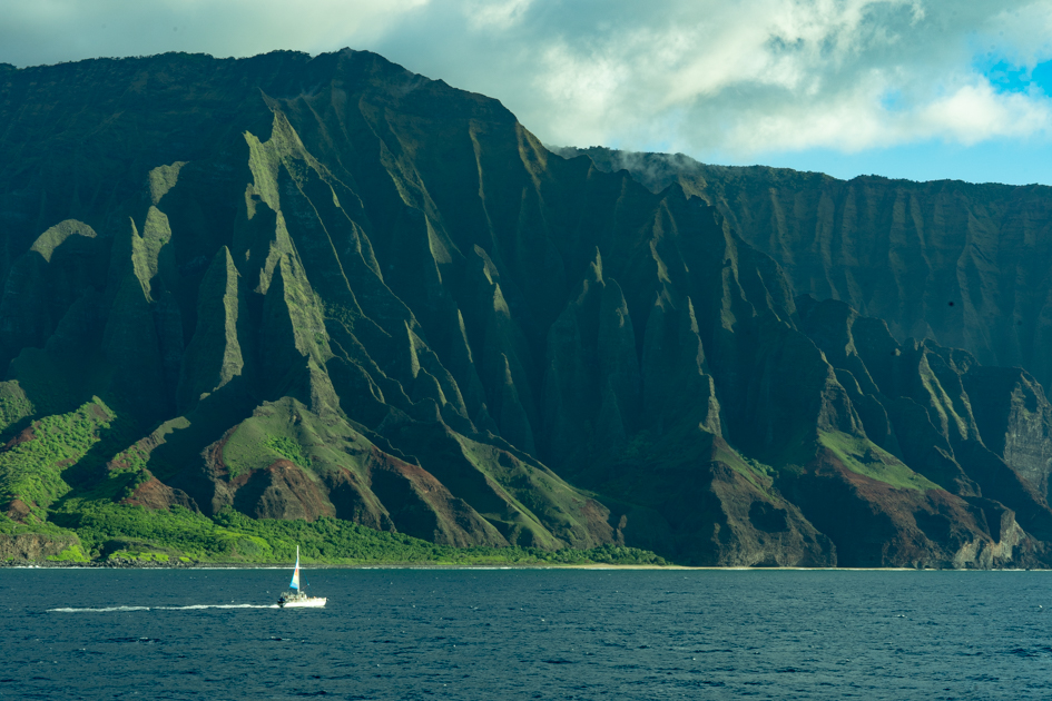Sailboat gliding in front of the Nā Pali Cliffs on Kauai’s north shore.