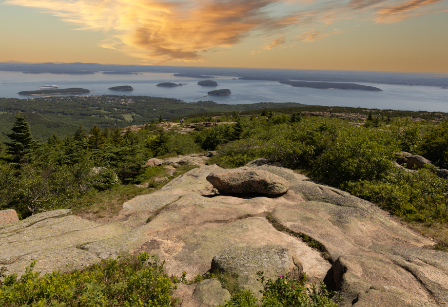 Golden sunrise from the summit of Cadillac Mountain in Acadia National Park with warm light spilling over the Atlantic Ocean.
