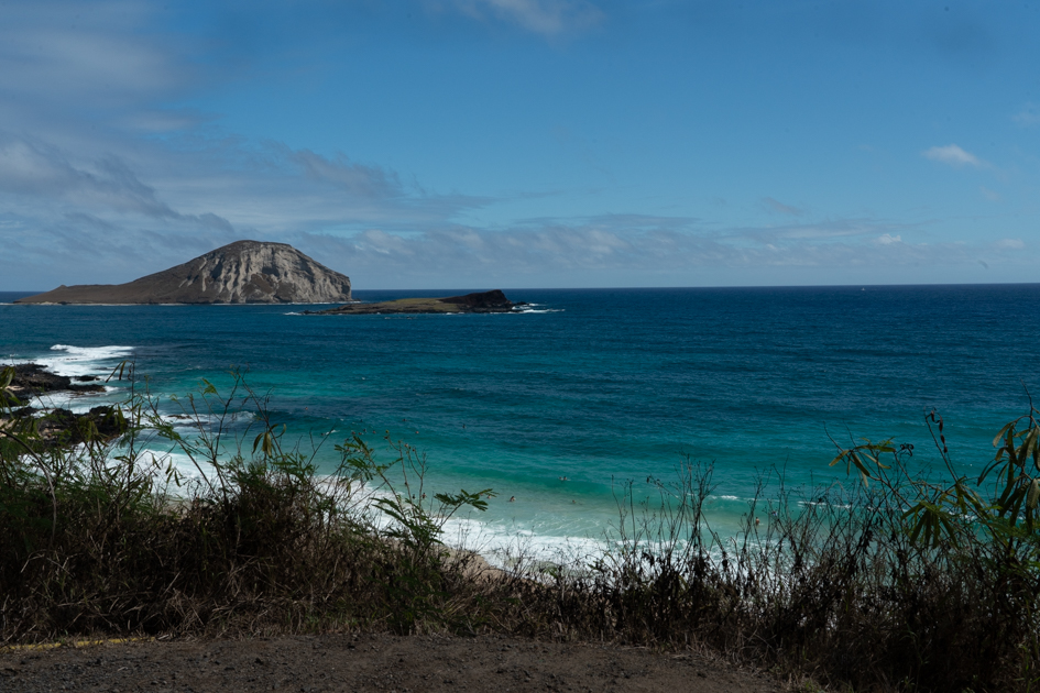 Golden sunrise light hitting the cliffs near Makapuʻu Point on Oahu, with soft clouds above the Pacific Ocean.

