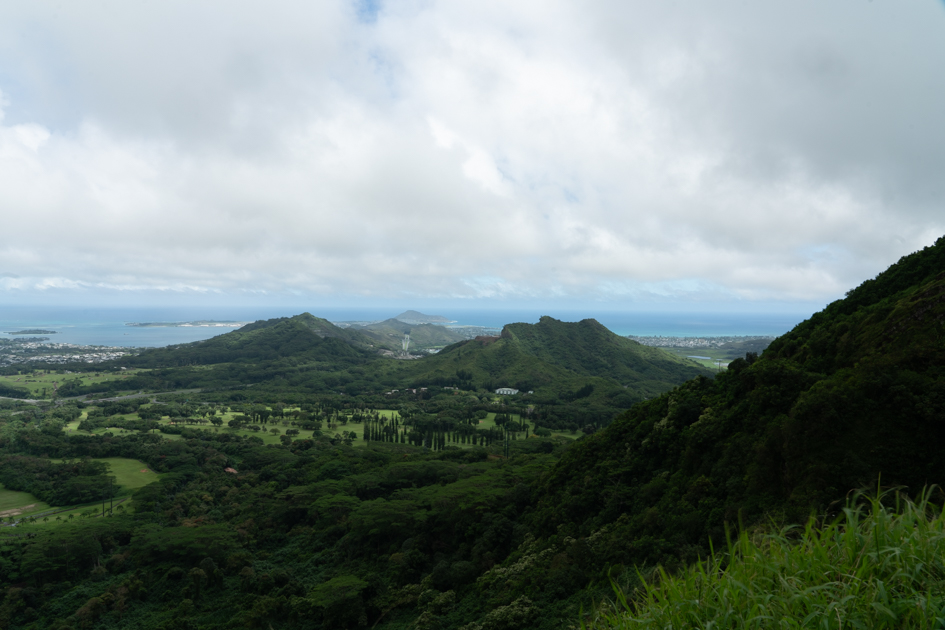 Wind sweeping through the cliffs at Nuʻuanu Pali Lookout with mist and dramatic light over the valley below.
