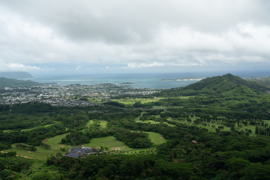 Panoramic view from Nuʻuanu Pali Lookout showing the lush Windward side of Oahu with clouds drifting over the Koʻolau Mountains.
