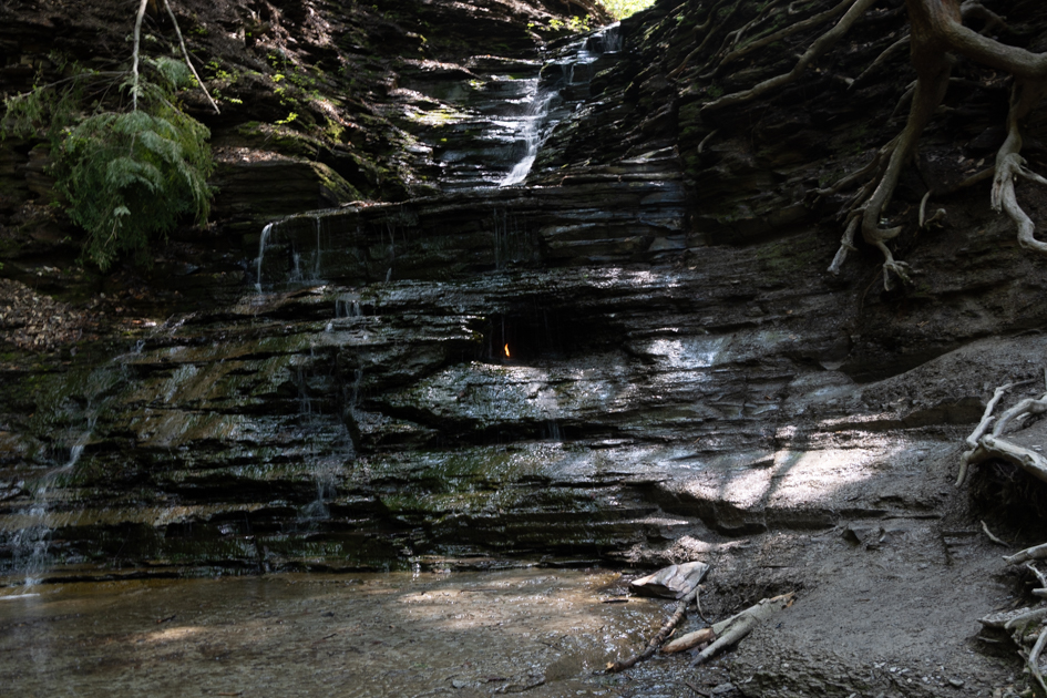 Water flowing over rocks at Eternal Flame Falls surrounded by shaded forest in Orchard Park, NY

