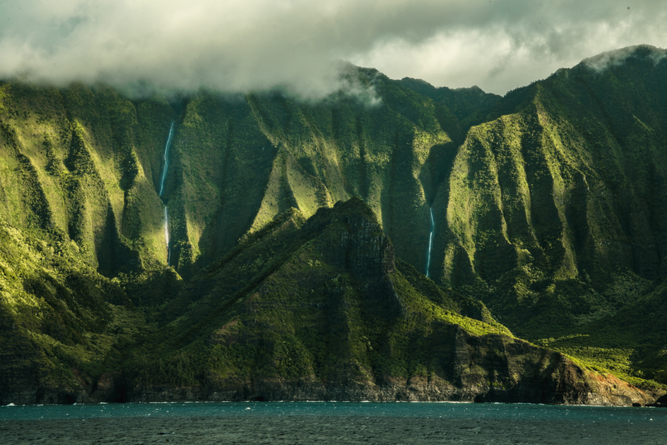 Waterfalls cascading down the green cliffs of the Nā Pali Coast after rainfall.