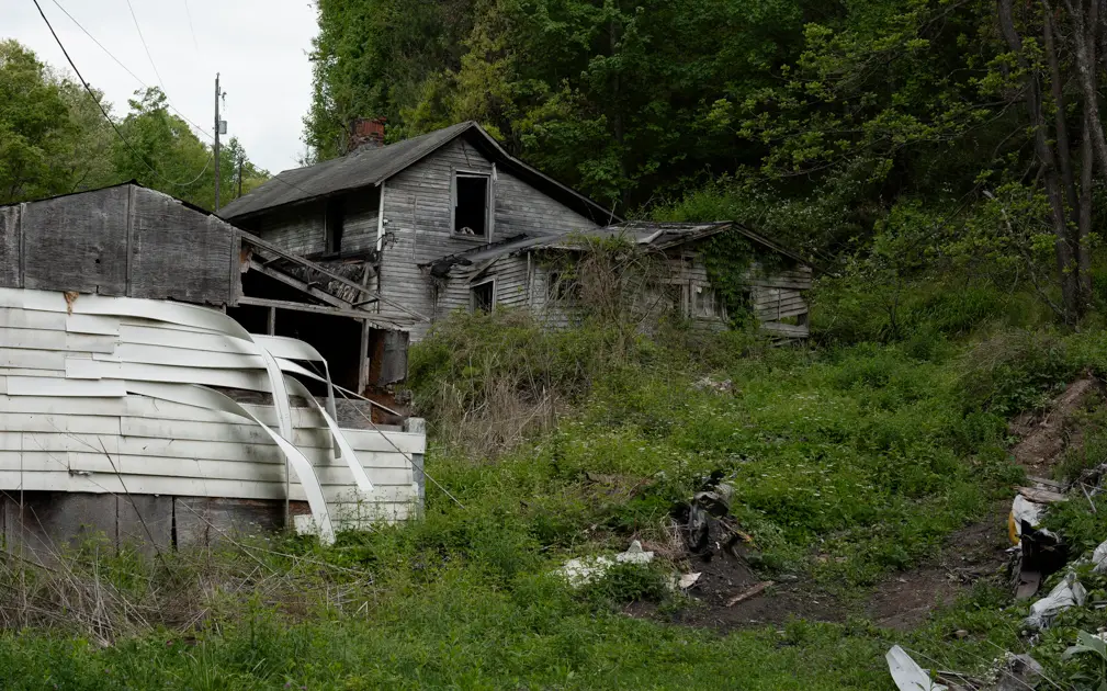 Abandoned house sitting deep in a quiet Appalachian holler surrounded by steep wooded hills.
