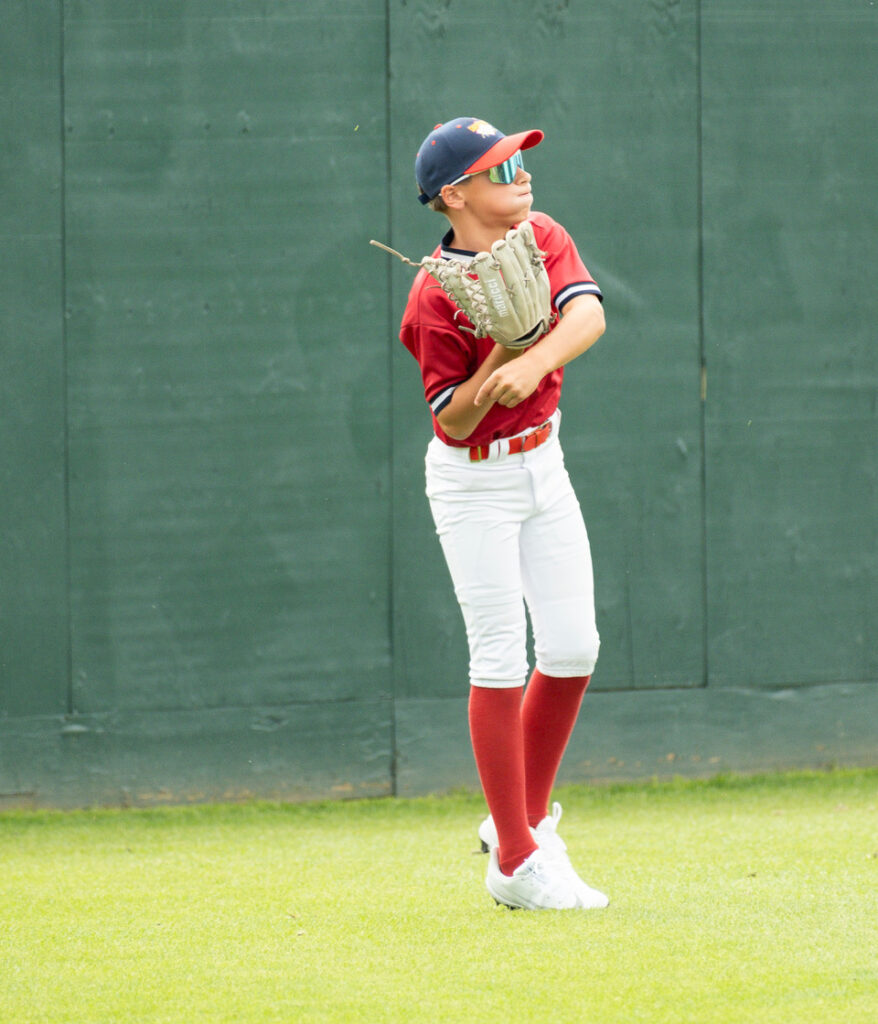 Youth baseball outfielder concentrating as he throws the ball at Cooperstown Dreams Park.
