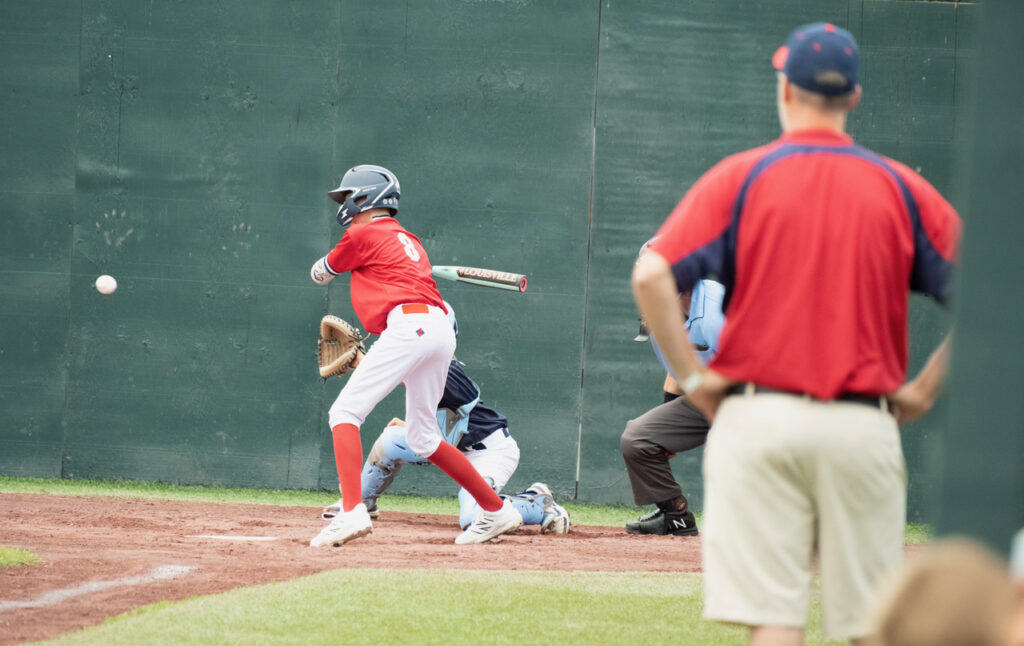 Youth baseball player making contact with the ball during a game at Cooperstown Dreams Park.