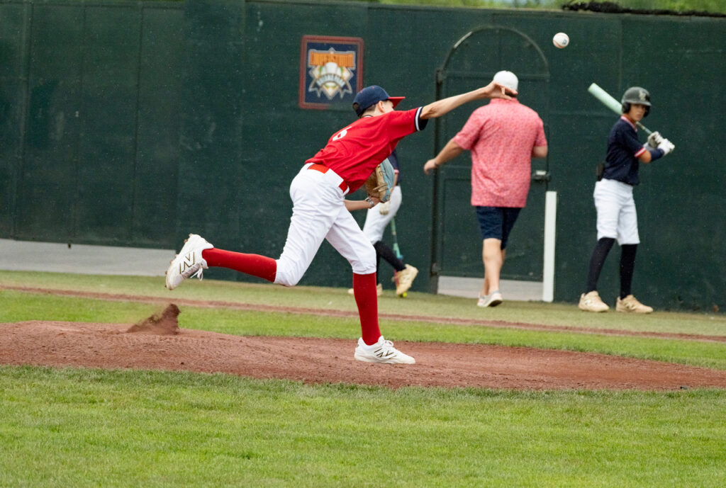 Youth baseball pitcher in mid-delivery while throwing a pitch at Cooperstown Dreams Park.

