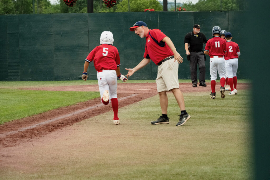 Coach giving high fives to youth baseball players after a home run at Cooperstown Dreams Park.