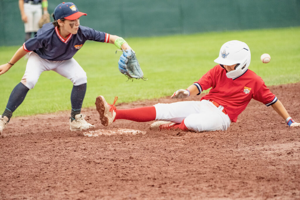 Youth baseball player sliding into base as the ball arrives at the fielder at Cooperstown Dreams Park.